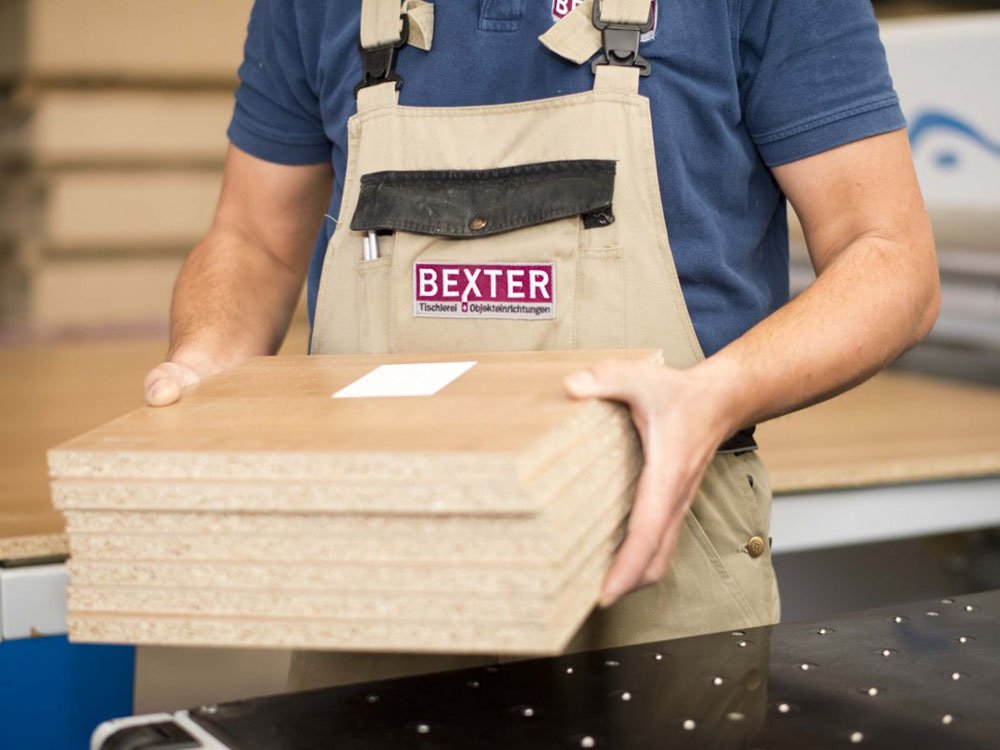 Mitarbeiter tr&auml;gt Holzplatten in der Werkstatt der Tischlerei Bexter